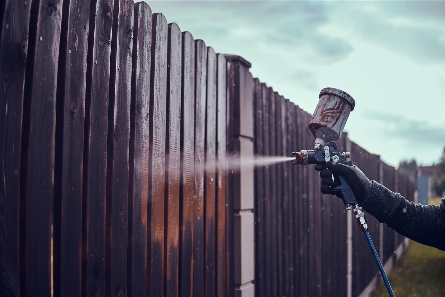 Spray technician refinishing an exterior fence with a spray system